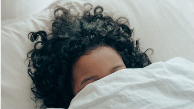 Vrouw die in bed ligt met de dekens over haar hoofd